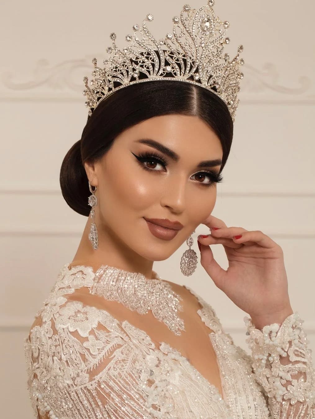 A sleek centre-parted chignon under an ornate crystal crown, with a lace gown