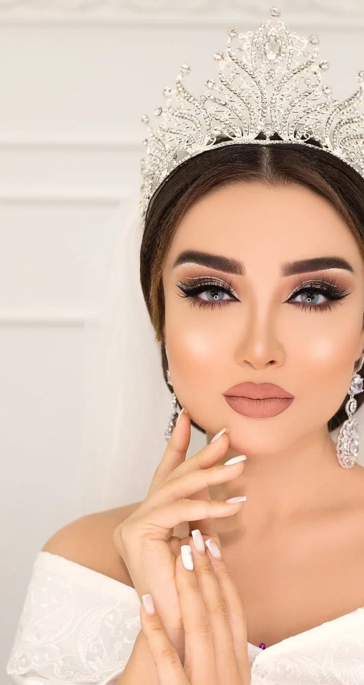 A bride under a soft tulle veil, in a nude lip and a lifted crystal crown